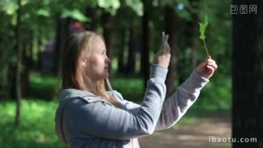 年轻女子在公园用她的手机拍绿叶的照片